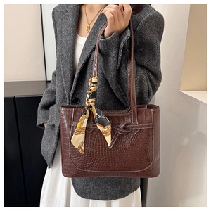 Detail of brown crocodile pattern tote bag with decorative silk scarf on handle
