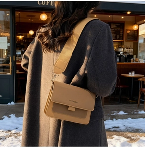 Close-up of khaki crossbody bag with wide strap and fashion lettering in street setting