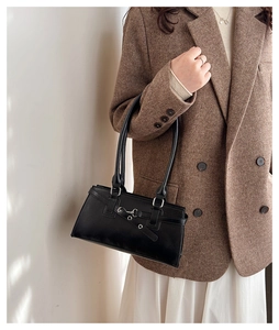 Detailansicht der schwarzen Vintage-Ledertasche mit Metallschnalle auf einem Tweed-Blazer