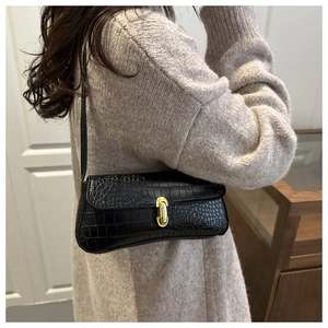 Sac baguette noir chic avec texture crocodile et fermoir doré porté à l'épaule