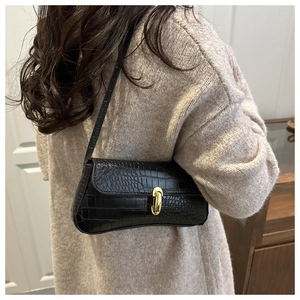 Detail of a black crocodile-pattern shoulder bag with a gold metal lock shown on a model