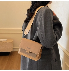 Close-up of khaki and brown crossbody bag with wide strap worn by a model in a room