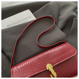 Détail d'un sac à bandoulière rouge motif crocodile avec un fermoir en métal doré en forme de U