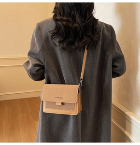 Rear view of a khaki and tan vintage small crossbody bag worn by a model in a warm room