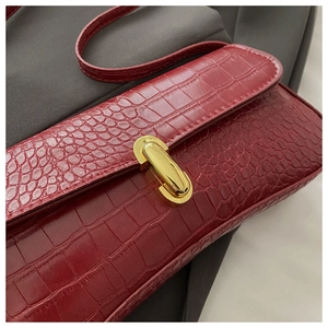 Gros plan sur la texture crocodile rouge vin et le fermoir en métal doré du sac