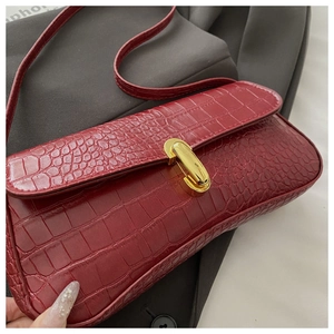 Détail de la texture cuir crocodile bordeaux et d'un fermoir ovale en métal doré