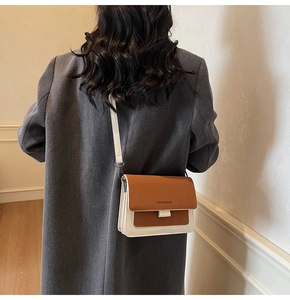 Detail of a brown and white contrast crossbody bag with accordion layers and lettering