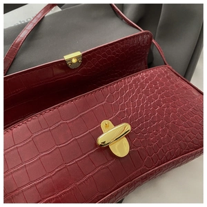 Détail du sac sous le bras en cuir crocodile rouge vin avec boucle en métal doré
