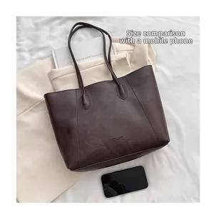 Close-up of dark brown tote bag showing leather texture and size comparison to phone
