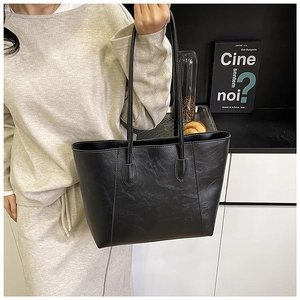 Detail of minimalist black tote bag with shoulder straps worn by model in beige knitwear