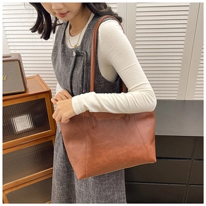 Detail view of large caramel brown leather tote bag worn on shoulder by a model