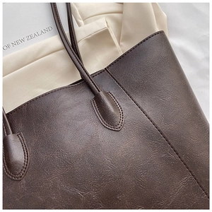 Macro detail of the dark brown tote bag showing textured PU leather and reinforced stitching