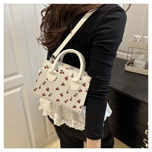 Close-up of a white leather crossbody bag with cherry prints on a model in a room