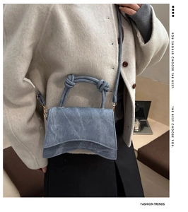 Detailed shot of denim handbag featuring a unique curved base and knotted rope handle