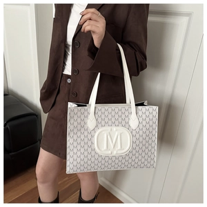 Detail of white tote bag featuring gray M-letter patterns and embossed central logo