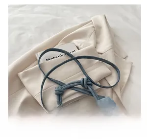 Close-up of light blue denim crossbody bag with knot handle and adjustable strap detail