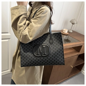 Detail shot of the embossed M logo on a black monogram tote bag with leather texture