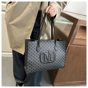 Close-up of a black tote bag featuring an embossed M logo and monogram patterns