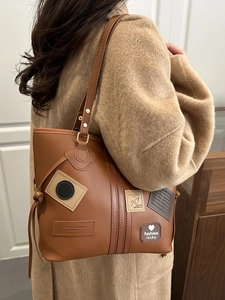 Classic large brown PU leather tote bag with vintage patches worn by a model