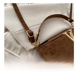 Detailed macro view of adjustable golden buckle and V-shaped logo on brown suede handbag