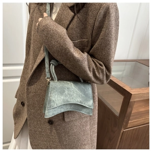 Detail of grey hourglass crossbody bag styled with a brown herringbone blazer on a model