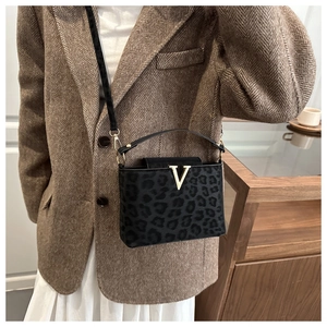 Détail du sac bandoulière léopard noir avec boucle dorée en V sur une surface en daim texturé