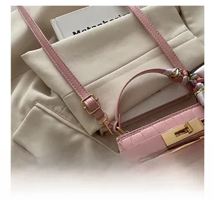 Detail of pink croc-effect handbag with gold hardware and colorful silk scarf handle