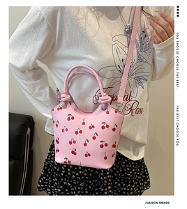 Dettaglio della borsa a secchiello rosa con stampe di ciliegie e trama in pelle PU