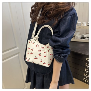 Detail showing white cherry print handbag in high-gloss leather with a round top handle