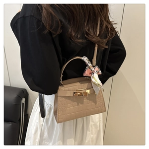 Close-up of a beige crocodile pattern handbag with gold clasp and silk scarf detail