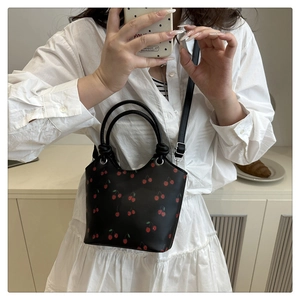 Dettaglio di una borsa a secchiello in ecopelle nera con stampe di ciliegie e doppi manici