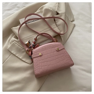 Detail of pink croc-embossed handbag featuring elegant silk scarf handle and gold buckle