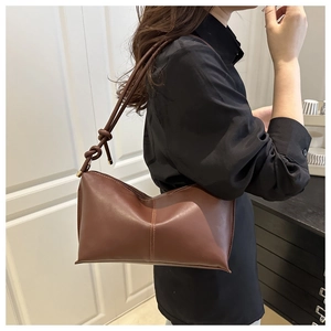 Close-up of brown matte leather handbag with vertical stitching and knotted shoulder strap