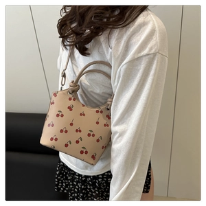 Detail of cream bucket bag with red cherry print featuring adjustable shoulder strap