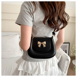 Detail of a black leather saddle bag with a gold metal bow on a model in a home setting