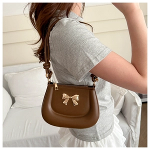 Detail of dark brown shoulder bag with golden bow and stylish knotted strap design
