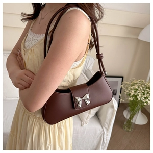 Detailed close-up of dark brown leather underarm bag with silver bow ornament