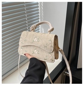 Macro detail of beige woven handbag featuring delicate floral embroidery and twisted handle