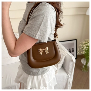 Detail of a brown leather shoulder bag with a gold metal bow and knotted strap design