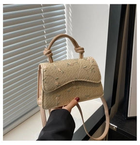 Close-up of beige woven bag featuring pink floral embroidery and knotted top handle