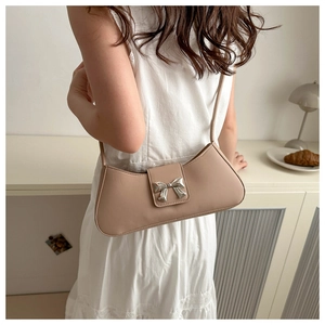 Dettaglio della borsa a tracolla beige con fibbia a fiocco argento indossata su abito bianco