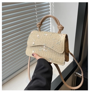 Detail of beige straw bag with pink floral embroidery and stylish knotted handle