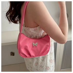 Gros plan d'un sac hobo rose avec détail papillon argenté porté par un mannequin femme