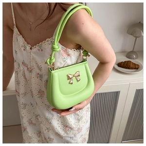 Detail of light green mini shoulder bag featuring a gold bow accent on leather texture