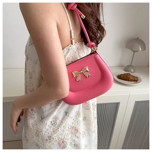 Close-up of a pink shoulder bag featuring a stylish golden metal bow decoration