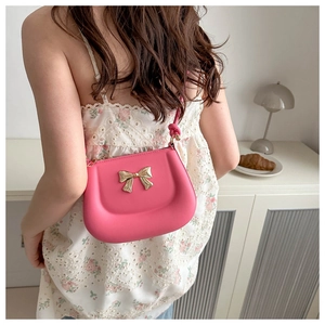 Detail of rose pink mini bag with gold bow buckle worn over a white lace dress