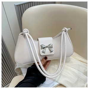Detail of an ivory baguette bag featuring a silver metal bow buckle and slim knot straps