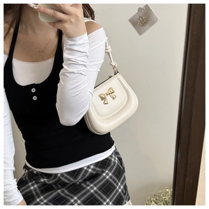 Detailed close-up of cream shoulder bag with elegant golden bow metal accent and round silhouette