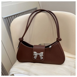 Detail of a brown PU leather baguette bag featuring a silver metal bow and knotted straps