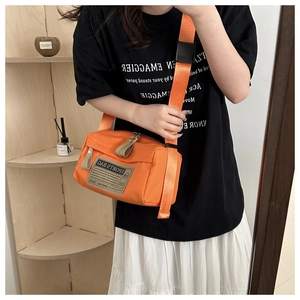 Detail of bright orange sports crossbody bag with vintage patch and metal zipper